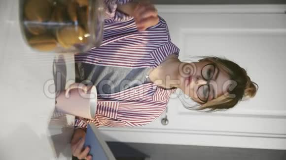 带眼镜的年轻美女在厨房里喝咖啡吃饼干和看书的垂直视频视频的预览图