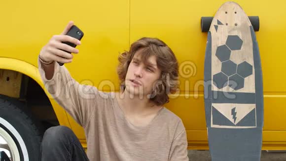 年轻的嬉皮士用手机坐在长板上视频的预览图