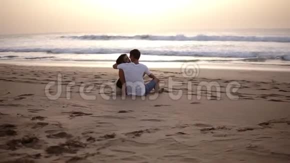 一对夫妇坐在沙滩上眺望大海在夕阳下亲吻两个相爱的场景视频的预览图