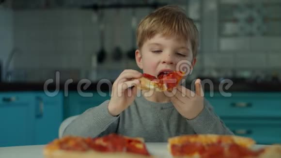 小男孩独自在蓝色厨房的家里吃披萨一个小孩在慢动作享受大披萨视频的预览图