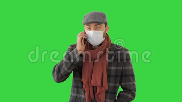 时尚男性带保护面具在绿色屏幕上行走在电话上交谈色度键视频的预览图