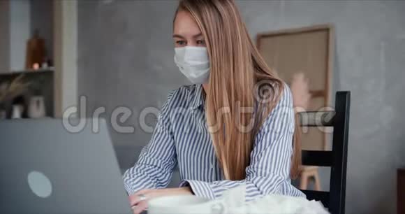 美丽的年轻金发医生女士使用笔记本电脑工作咨询人们从家里自我隔离戴着面罩视频的预览图