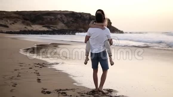 恋爱中的情侣穿着衬衫的男人在海滩上转过他可爱的女人完整的光脚少年快乐观视频的预览图