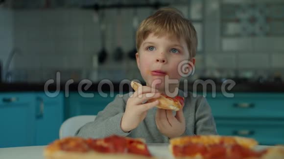 小男孩独自在蓝色厨房的家里吃披萨一个小孩在慢动作享受大披萨视频的预览图