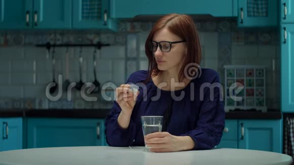 30多岁的年轻女性戴着眼镜在家里的厨房里慢动作地吃维他命和药片还有一杯水视频的预览图