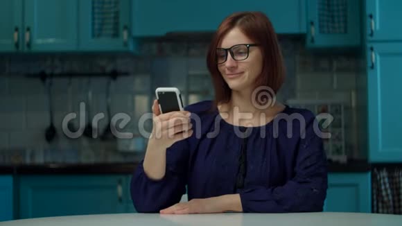 30多岁的年轻女性戴眼镜在检疫期间通过手机应用程序在家厨房进行在线订购妇女收到视频的预览图
