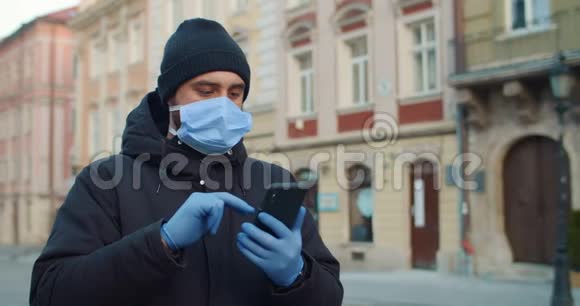 男人在使用智能手机时戴着医用口罩和手套打字一个戴着防护面具的人独自站着视频的预览图