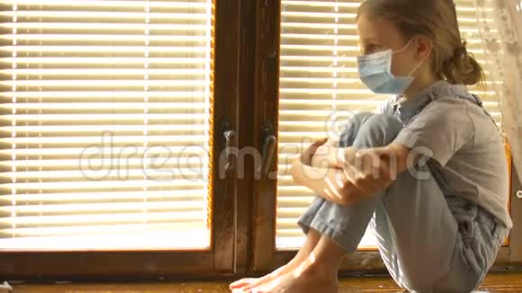 厌倦了无聊的小女孩正坐在窗台上戴着一次性防护面罩在自我孤立的时候视频的预览图