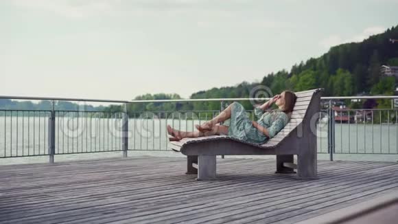 布鲁内特女士穿着浪漫的裙子在湖边的日光躺椅上放松太阳眼镜视频的预览图