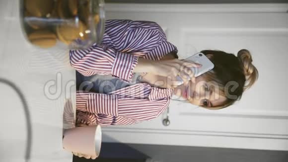 垂直视频年轻微笑的女人喝咖啡在厨房打电话视频的预览图