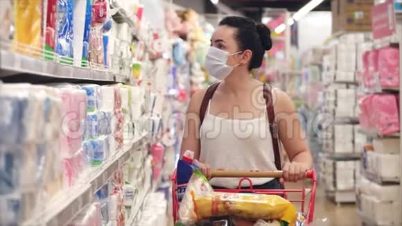 戴着冠状病毒流行面具的年轻女孩或妇女在超市买卫生纸人们在超市里恐慌地买卫生纸视频的预览图