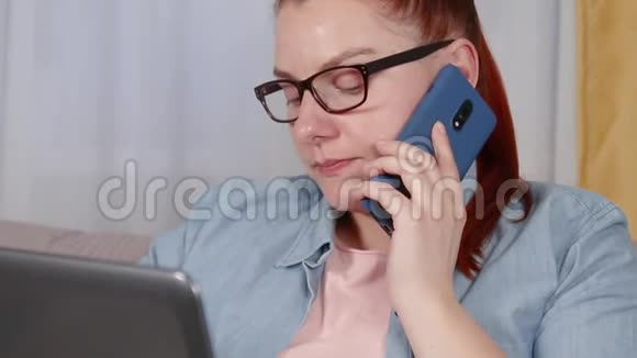 一个疲惫的年轻女人坐在客厅里用笔记本电脑工作的肖像女人用手机说话视频的预览图