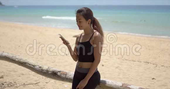 在海滩上的智能手机上讲话的性格开朗的民族女运动员视频的预览图