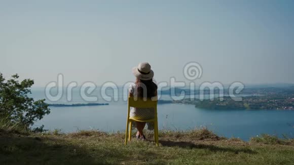 戴帽子的年轻女子坐在山上的椅子上休息看风景的湖景视频的预览图