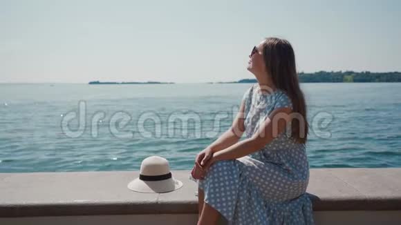 戴墨镜的女人坐在帽子附近靠在嘉达湖畔的石墩上视频的预览图