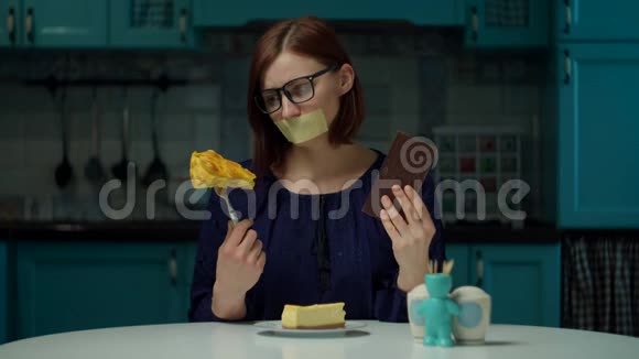 30岁的年轻黑发女人戴着眼镜嘴上贴着胶带坐在家里手里拿着糖果闻着巧克力的味道视频的预览图