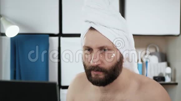 人从脸上剥去补丁一个穿着毛巾长着迷人胡须的男人看着镜子摘下视频的预览图