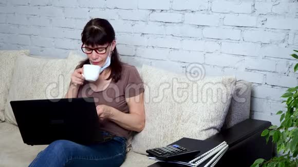 从家里远程工作成年白种人妇女正在沙发上的客厅里用笔记本电脑做保护性医疗视频的预览图