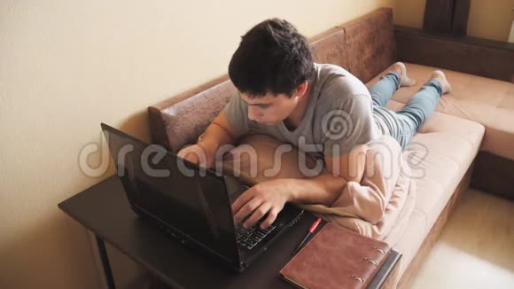一个自由职业者躺在床上在家里用笔记本电脑工作男人用手在笔记本键盘上打字视频的预览图