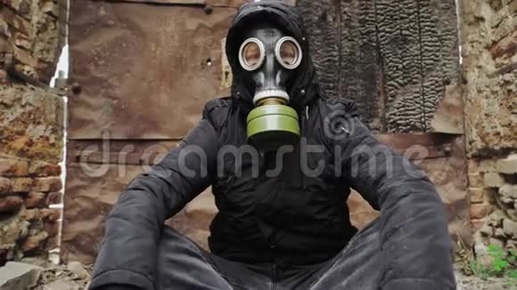 戴着防毒面具和黑色帽衫的人坐在一座被毁的废弃建筑的背景上后世界末日视频的预览图