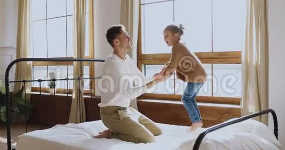 快乐坦率可爱的小女孩在卧室里和爸爸玩视频的预览图