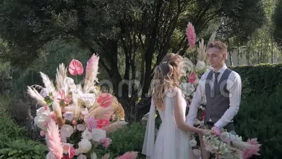 美丽的潘潘草和玫瑰拱门新娘和新郎在婚礼拱门的背景上互相看着视频的预览图