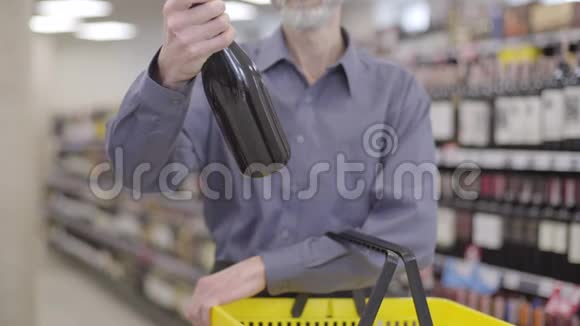 面目全非的大胡子老人看着酒瓶把它放进黄色的购物篮男性客户视频的预览图
