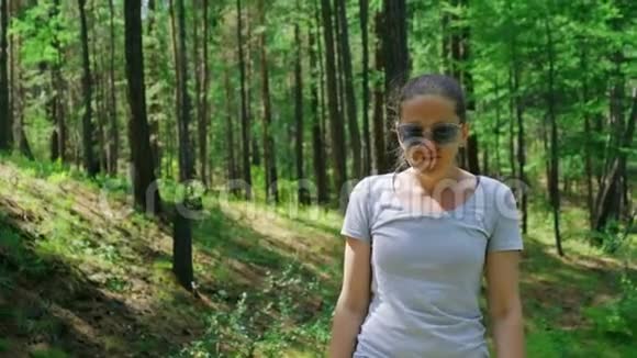戴着蓝色眼镜的女孩走在绿色的森林里慢动作4K视频的预览图