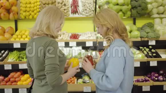两个成年女人带着红色和黄色的甜椒说话对着镜头微笑白人女性正面肖像视频的预览图