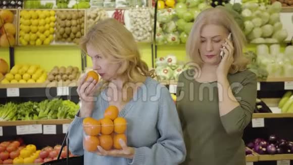 漂亮的高白种人女人闻着新鲜美味的橘子就像她的女朋友在电话里说话一样积极正面视频的预览图