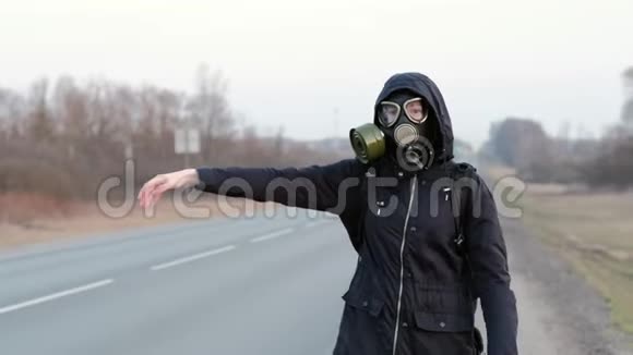 COVID19一个穿着深色衣服戴着防毒面具的女孩在阴天站在路边视频的预览图
