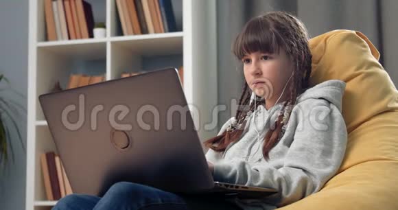 十几岁的孩子坐在黄豆袋椅子上用笔记本电脑视频的预览图