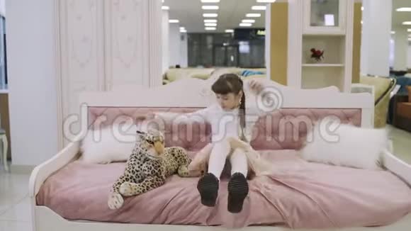 漂亮的少女坐在家具店的粉红色儿童床上在购物中心挑选家具的年轻女孩视频的预览图