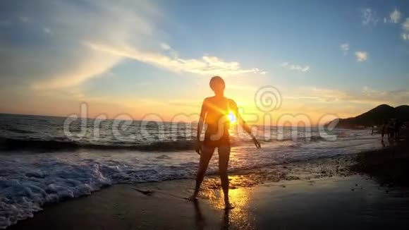 年轻快乐的女人在海浪的沙滩上跳跃着金色的夕阳背景视频的预览图