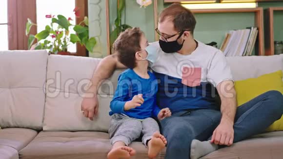 在镜头前小男孩和他的父亲呆在家里隔离他们戴着保护面具用这个孩子视频的预览图