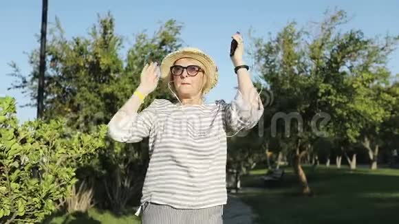 六十岁快乐女人的肖像戴着耳机唱着歌视频的预览图