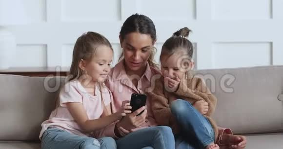 年轻漂亮的女人给小孩子姐妹播放有趣的视频视频的预览图