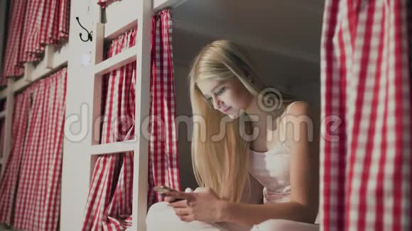 年轻漂亮的女人坐在宿舍的床上用智能手机视频的预览图