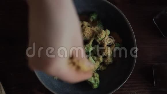 女孩用手在厨房的餐桌上用碗里的香料混合着西兰花从上面看视频的预览图