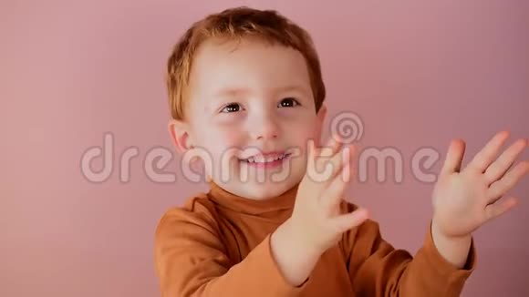 可爱的小红头发男孩微笑着双手拍在粉红色的背景上视频的预览图