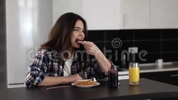 检疫期间厨房里的年轻女子女孩坐在桌子旁吃带果酱的烤面包享用早餐或早晨视频的预览图