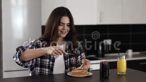 检疫期间厨房里的年轻女子呆在家里的桌子上在烤面包上放一些带刀的果酱美味可口视频的预览图