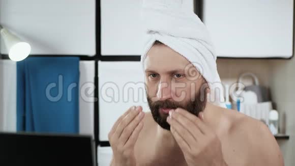 男人脸上涂奶油一个满脸胡须的白种人头上戴着毛巾用皱纹霜保湿视频的预览图