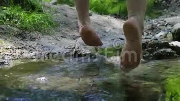 女孩坐在小溪上的木桥上光着脚在水里晃来晃去视频的预览图