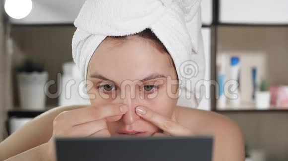 女孩捏着鼻子上的黑点有魅力的女人头上戴着毛巾照镜子把皮肤压在上面视频的预览图