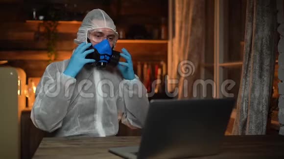 穿着工作服护目镜和医用呼吸器的年轻人在笔记本电脑上打字视频的预览图