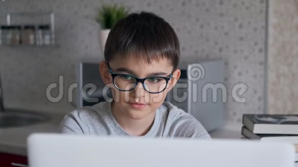 肖像一个小学生在家里坐在餐桌旁的厨房里看着桌子上的笔记本电脑做作业视频的预览图