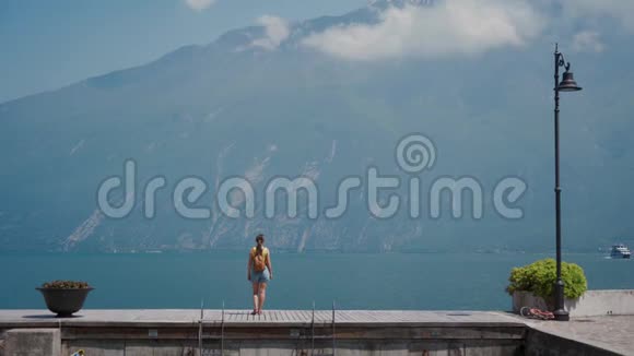 游客背着背包站在石墩上欣赏阿尔卑斯山的湖景视频的预览图