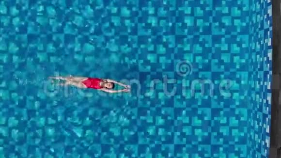 美丽的女士穿着红色比基尼背部游泳在蓝色游泳池放松假期概念空中小牛肉视频的预览图