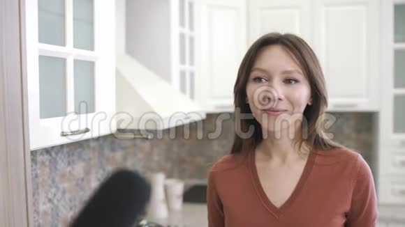 在采访记者时快乐的年轻女子记者带着麦克风采访女孩在家厨房博客视频的预览图